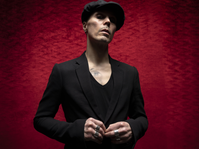 HIM frontman Ville Valo standing against a burgundy red background