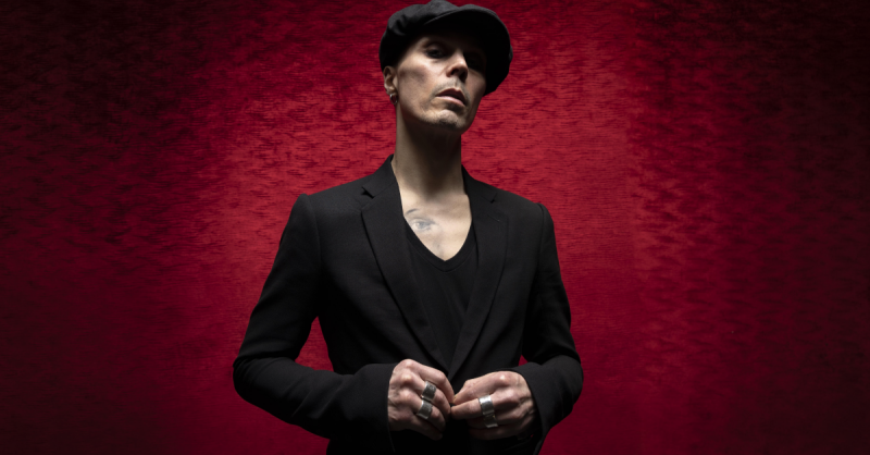 HIM frontman Ville Valo standing against a burgundy red background